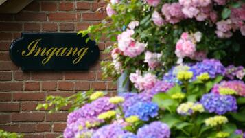 A brick wall with a sign that reads "Ingang" and a variety of colorful flowers.