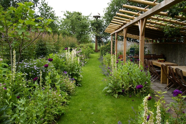 A garden with a wooden pergola, a pathway, and various plants and flowers.