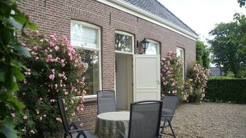 A brick house with a gravel driveway, a round table with four chairs, and pink flowering bushes.