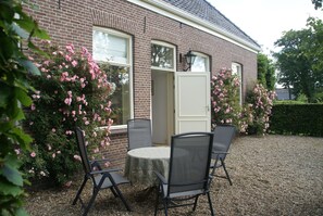 A brick house with a gravel driveway, a round table with four chairs, and pink flowering bushes. - De Heerlijkheid Ruinerwold (Ruinerwold)