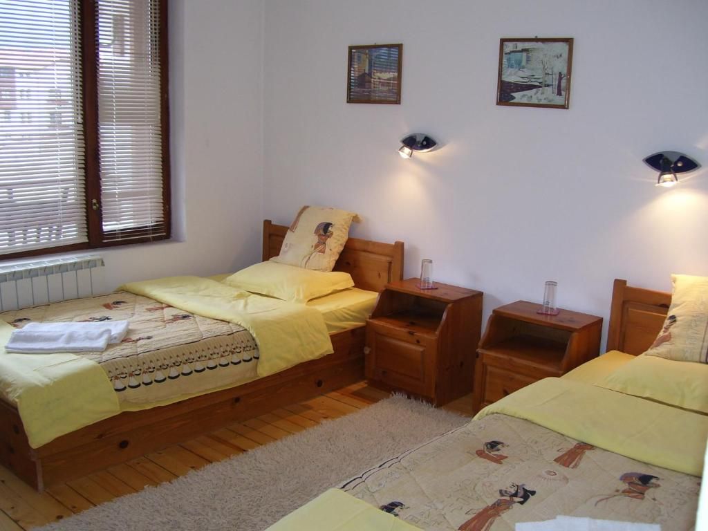 Een slaapkamer met twee houten bedden, een raam met zonwering en twee wandlampen.