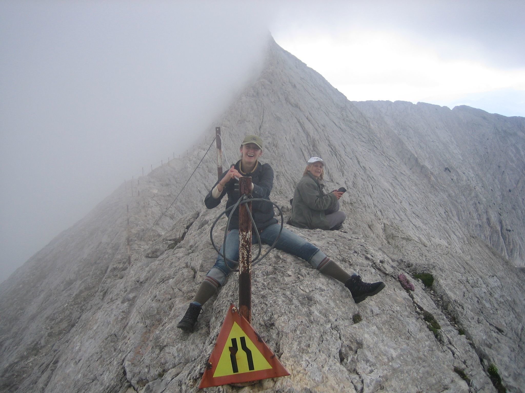 Two people on a rocky mountain with a warning sign.