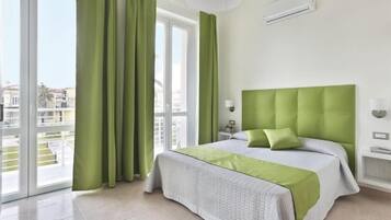 Habitación de hotel con una cama, cortinas verdes, una ventana y un equipo de aire acondicionado.