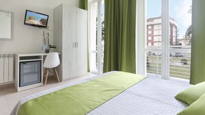 Un dormitorio moderno con cama, escritorio, silla, televisor y vistas al exterior.