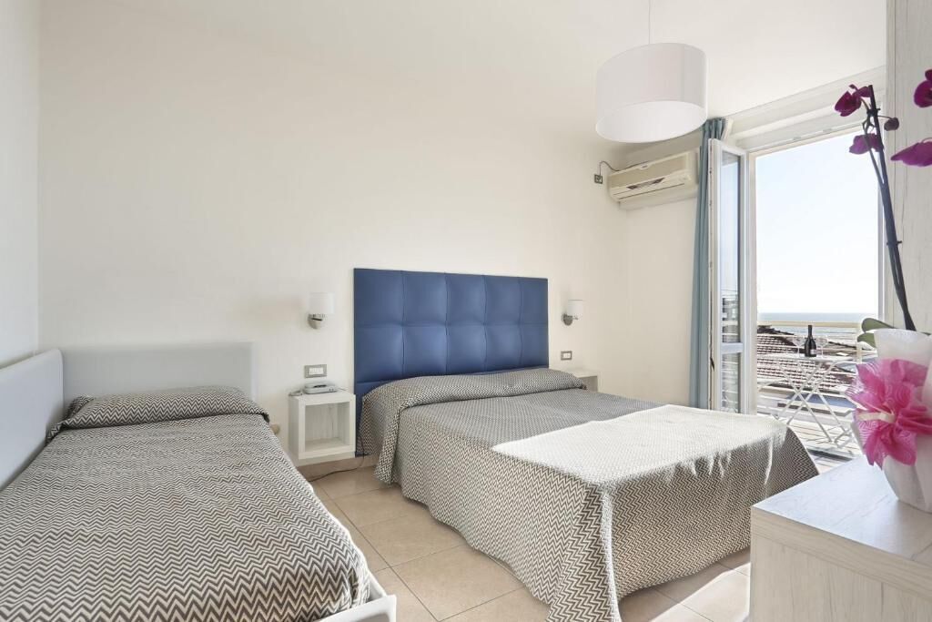 Een hotelkamer met twee bedden, een groot raam en uitzicht op het strand.
