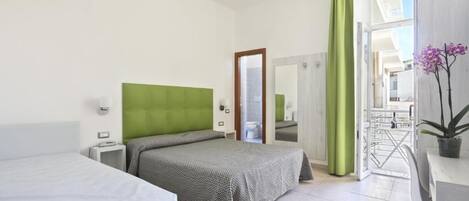 A hotel room with a bed, a desk, a chair, a mirror, and a view of the outside.