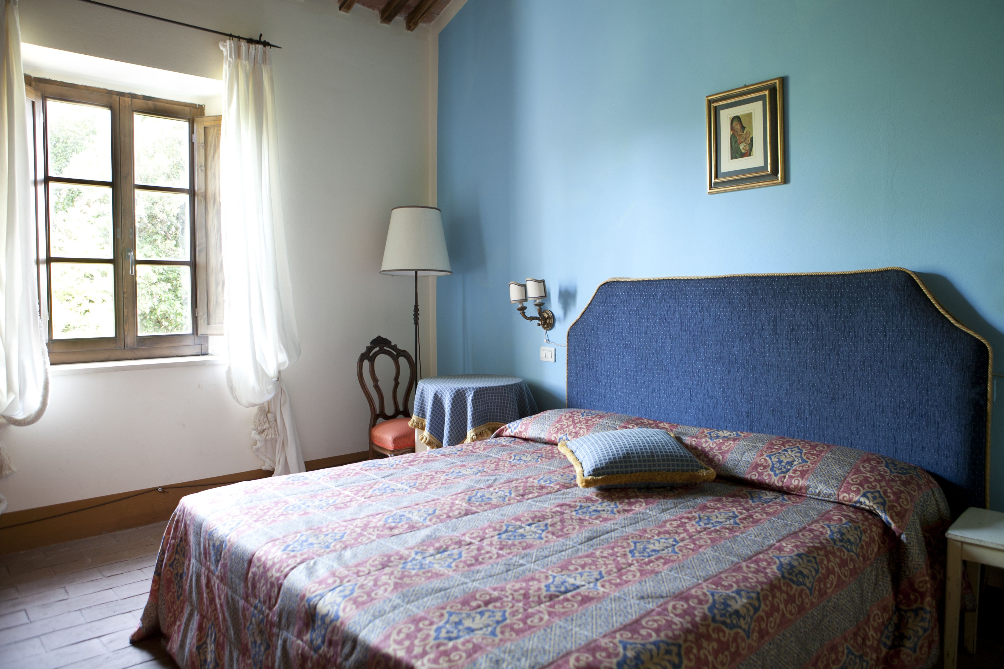 A bedroom with a bed, a window with curtains, a bedside table, and a lamp.