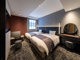 Una habitación de hotel moderna con dos camas, un ventanal grande, un espejo redondo y una pequeña zona de estar.