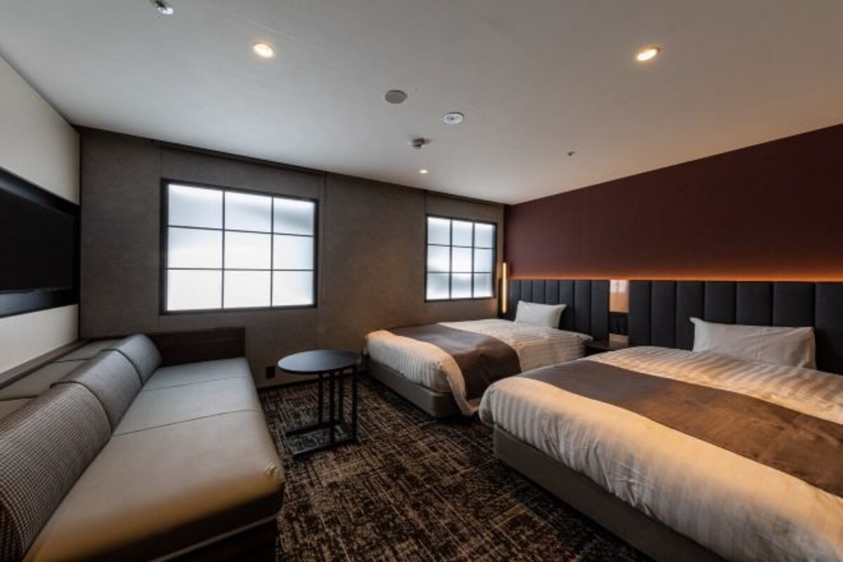 Una habitación de hotel moderna con un sofá, dos camas, una mesita y ventanas amplias.