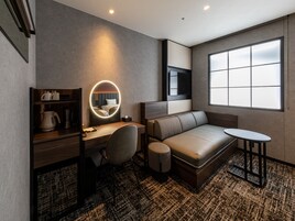 Una habitación de hotel moderna con cama, escritorio, silla y un espejo redondo con iluminación.