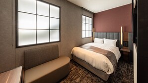Una habitación de hotel moderna con una cama grande, un banco y un amplio ventanal.