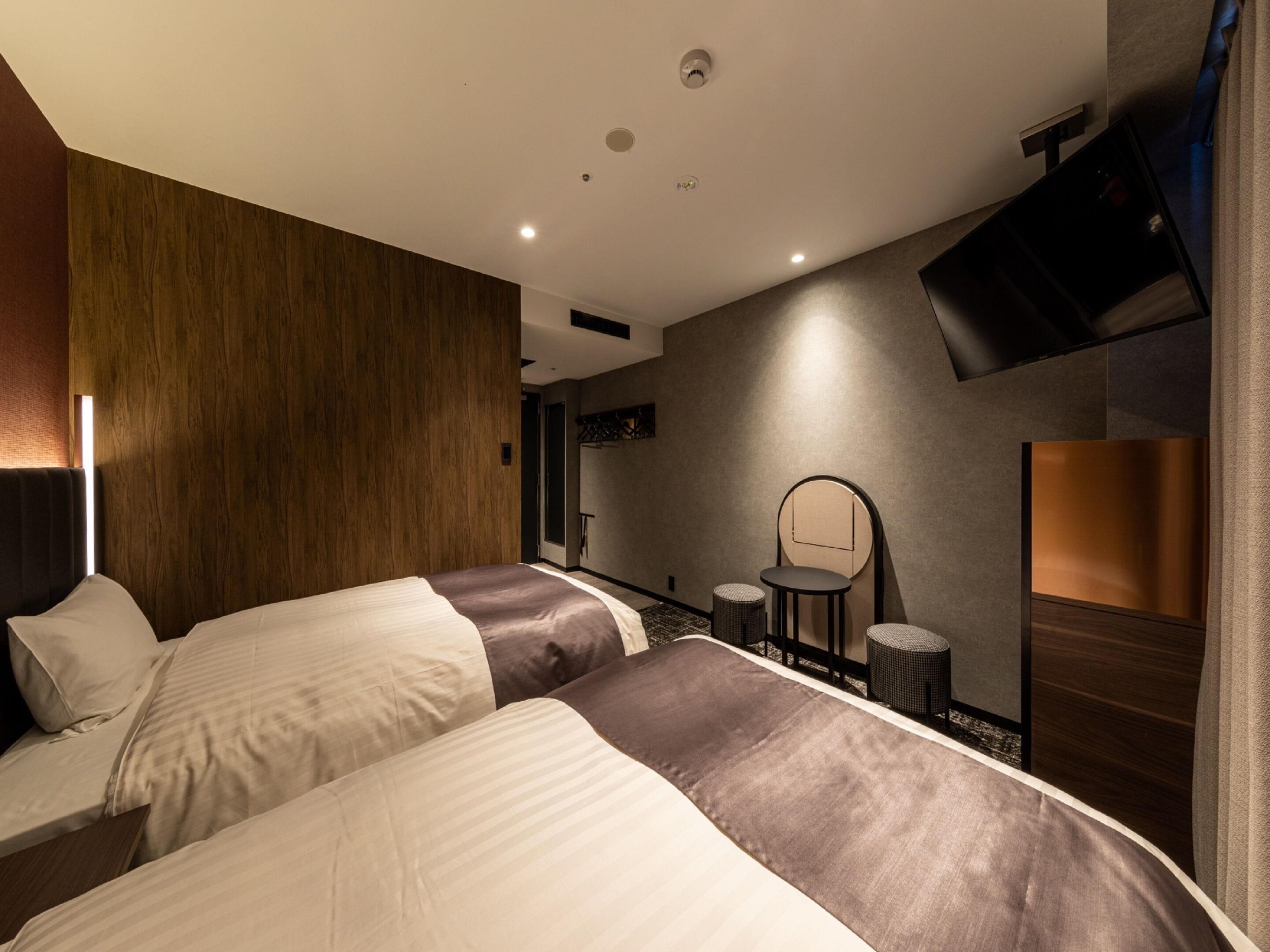 A modern hotel room with two beds, a TV mounted on the wall, and a small table with chairs.