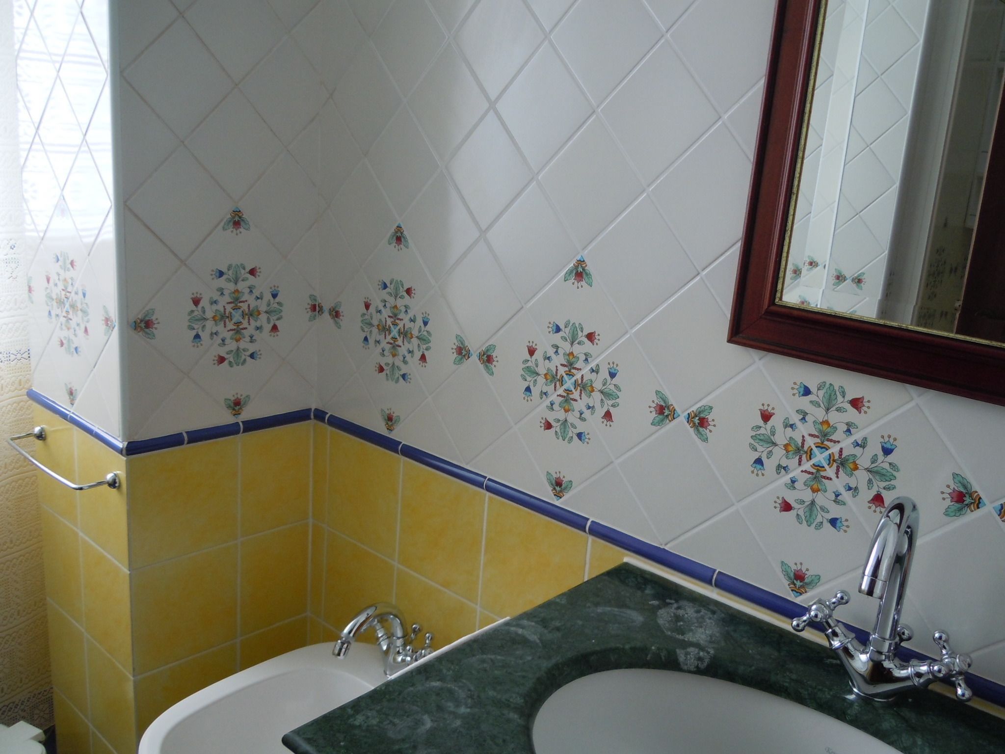 Ein Badezimmer mit einem weißen Waschbecken, gelb-blauen Fliesen und einem floralen Muster an der Wand.