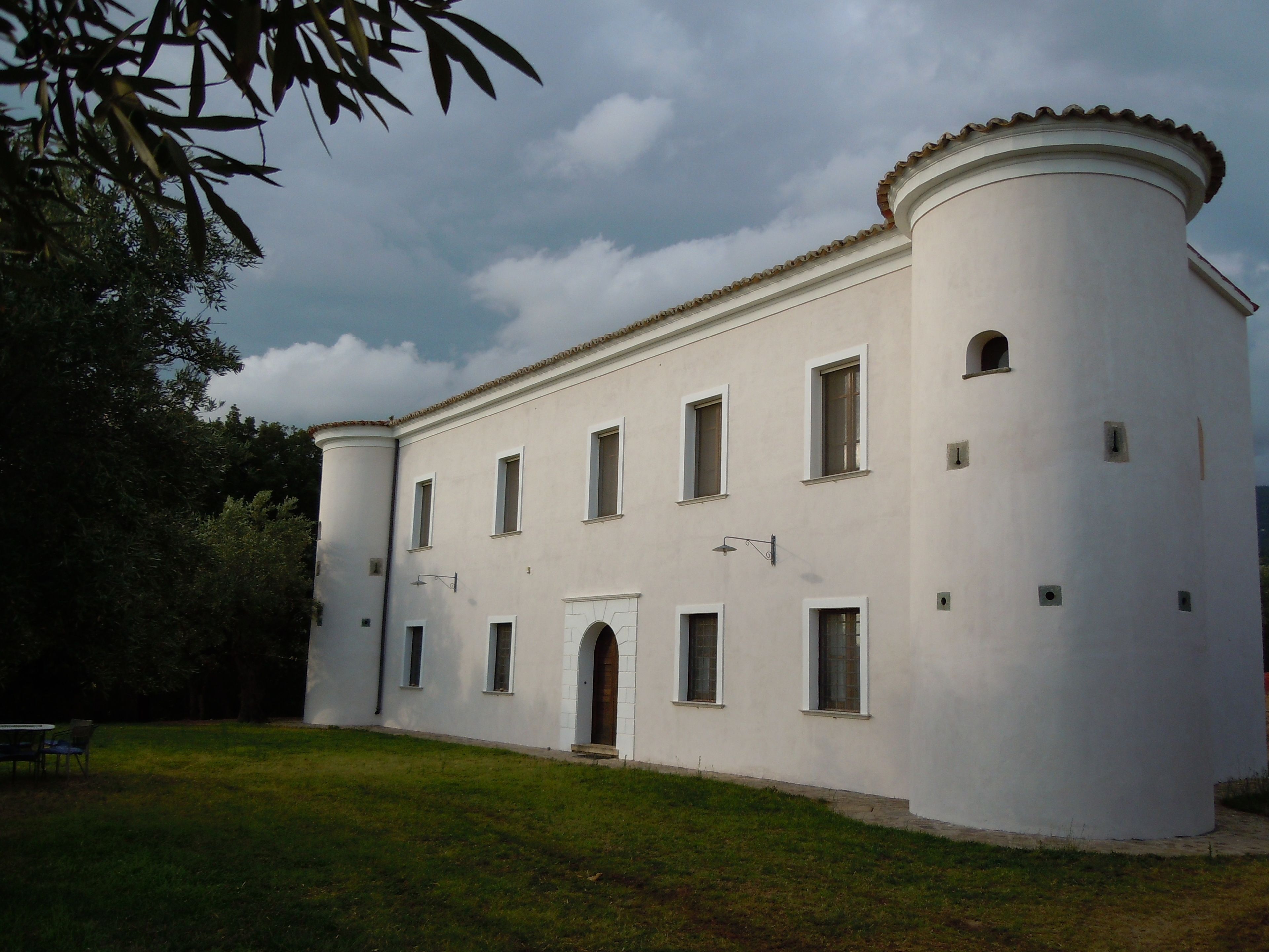 A white building with a round tower, multiple windows, and a small entrance.