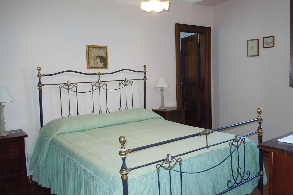 A bedroom with a metal-framed bed, a wooden door, and a small bedside table with a lamp.