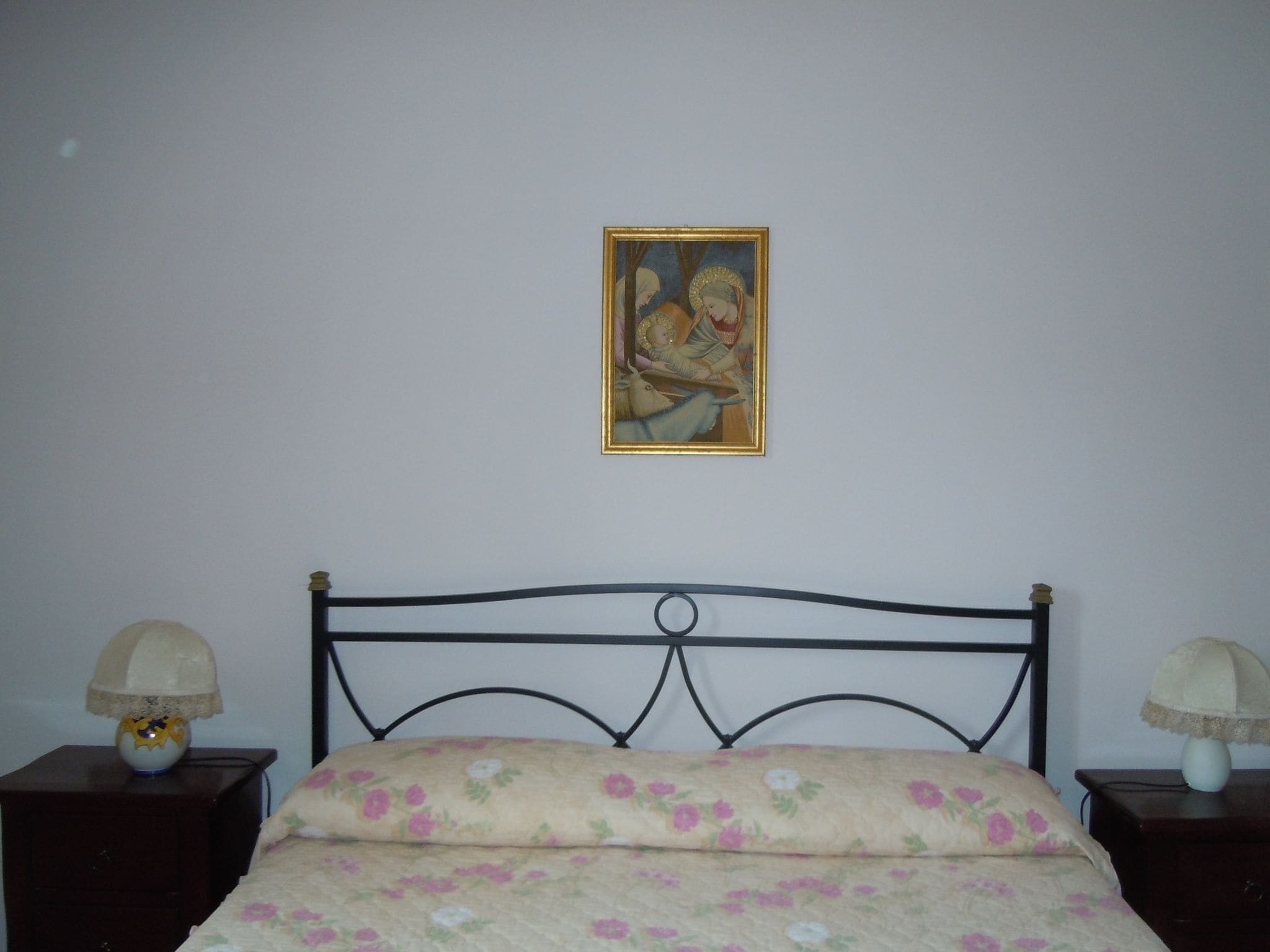 Un dormitorio con una cama, dos mesitas de noche, un cuadro en la pared y una lámpara en cada mesita.
