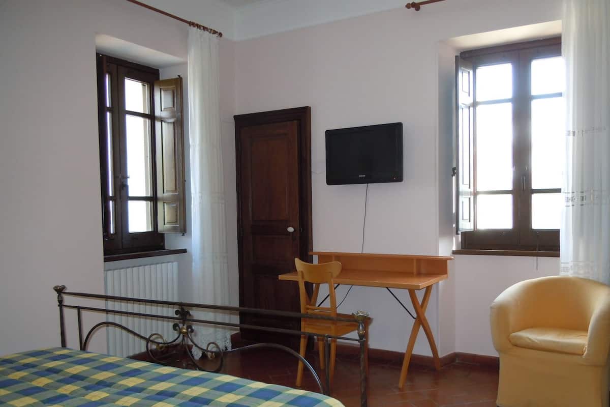 A room with a bed, a desk, a chair, a television, and windows.