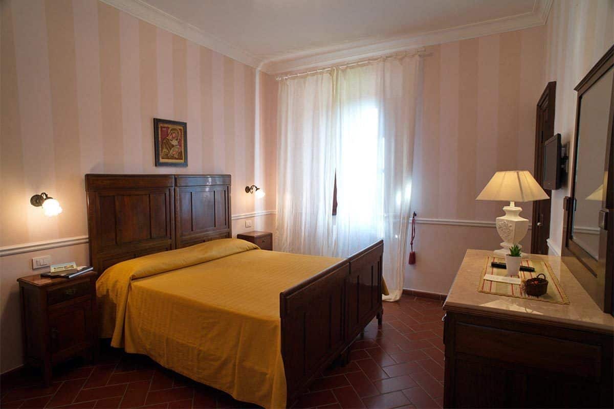 A hotel room with a wooden bed, a nightstand, a bedside table, a lamp, and a mirror.