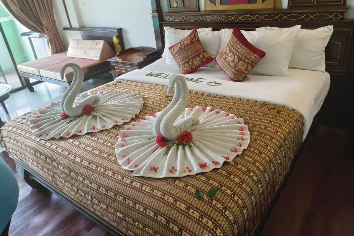 Habitación de hotel con cama, dos toallas con forma de cisne, cabecero de madera y ropa de cama estampada.