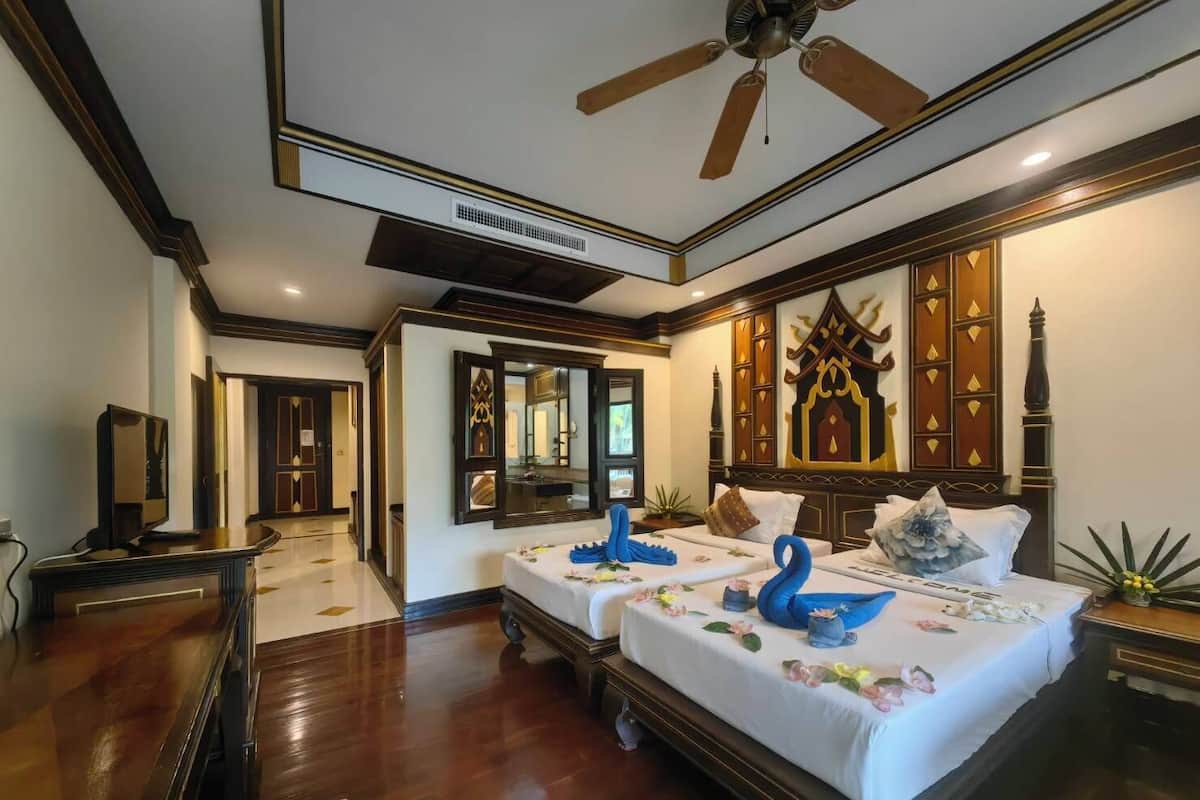 A hotel room with two beds, a ceiling fan, and traditional decor.