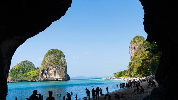 Una playa vista desde la entrada de una cueva, con agua azul cristalina y acantilados rocosos.