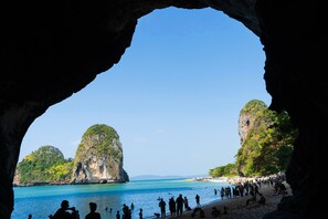 Une plage, vue à travers l’entrée d’une grotte, avec une eau d’un bleu limpide et des falaises rocheuses.