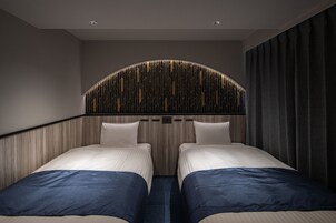 A hotel room with two beds, a curved headboard, and a dark curtain.