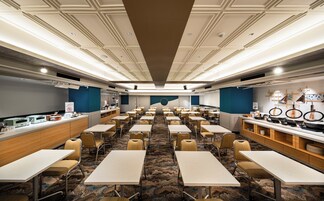Un salón de conferencias con filas de mesas y sillas, una zona de kitchenette y una pared grande con un diseño circular.