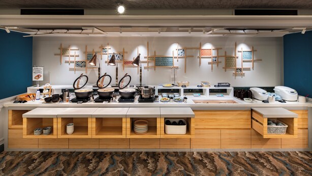 A modern kitchen area with a long counter, various kitchen appliances, and storage cabinets. - Dotonbori Hotel (Osaka)