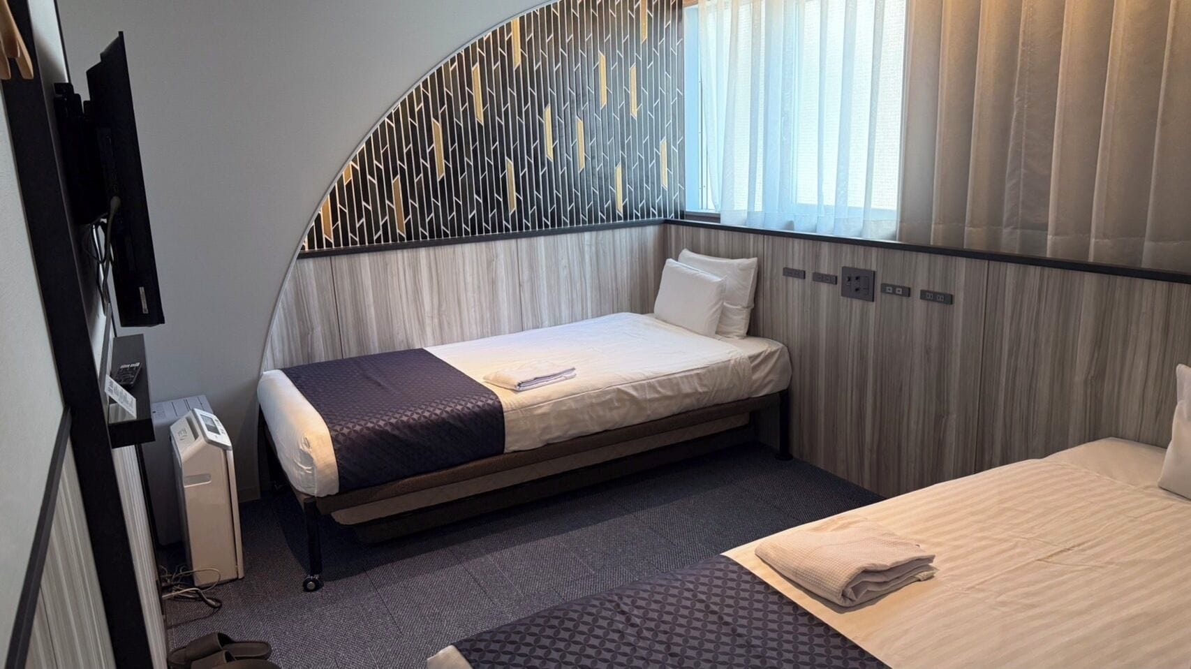 A compact hotel room with a single bed, a small desk, and a window with curtains.