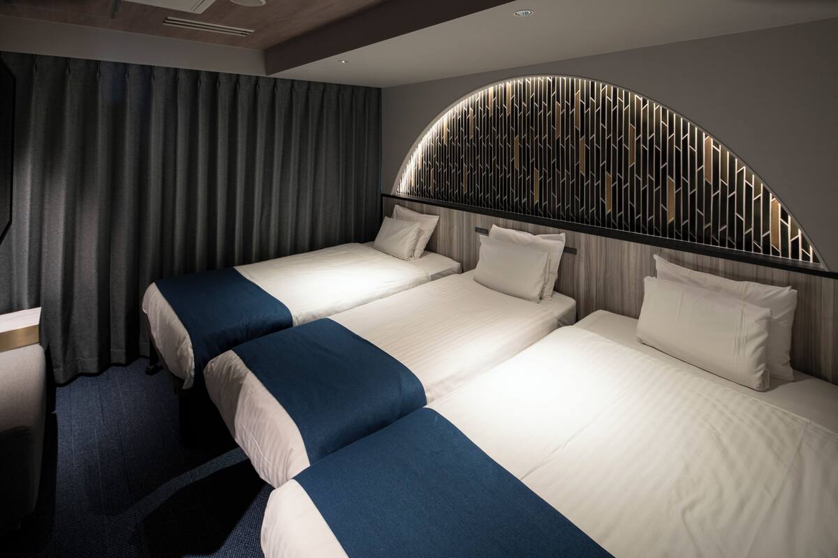 A hotel room with two beds, a curved headboard, and a large window with curtains.