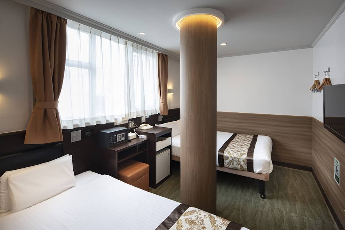 A hotel room with a large bed, a desk with a telephone, a small refrigerator, and a bedside table.
