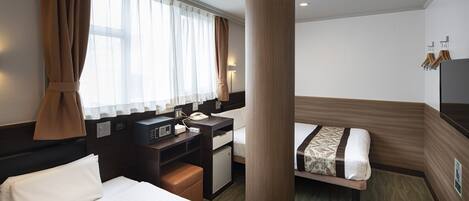 A hotel room with a large bed, a desk with a telephone, a small refrigerator, and a bedside table.