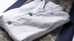A neatly folded white towel with a button detail, placed on a patterned bedspread. - Dotonbori Hotel (Osaka)
