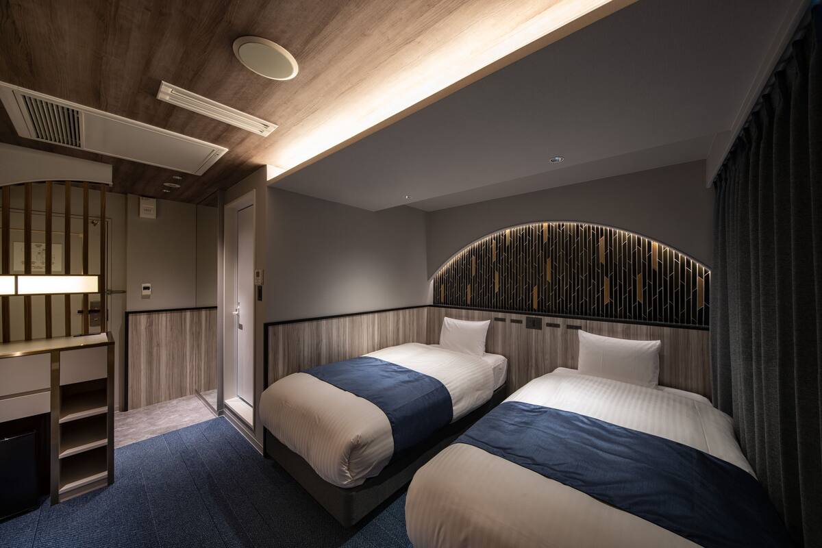 A modern hotel room with two beds, a built-in desk, and a unique curved headboard.