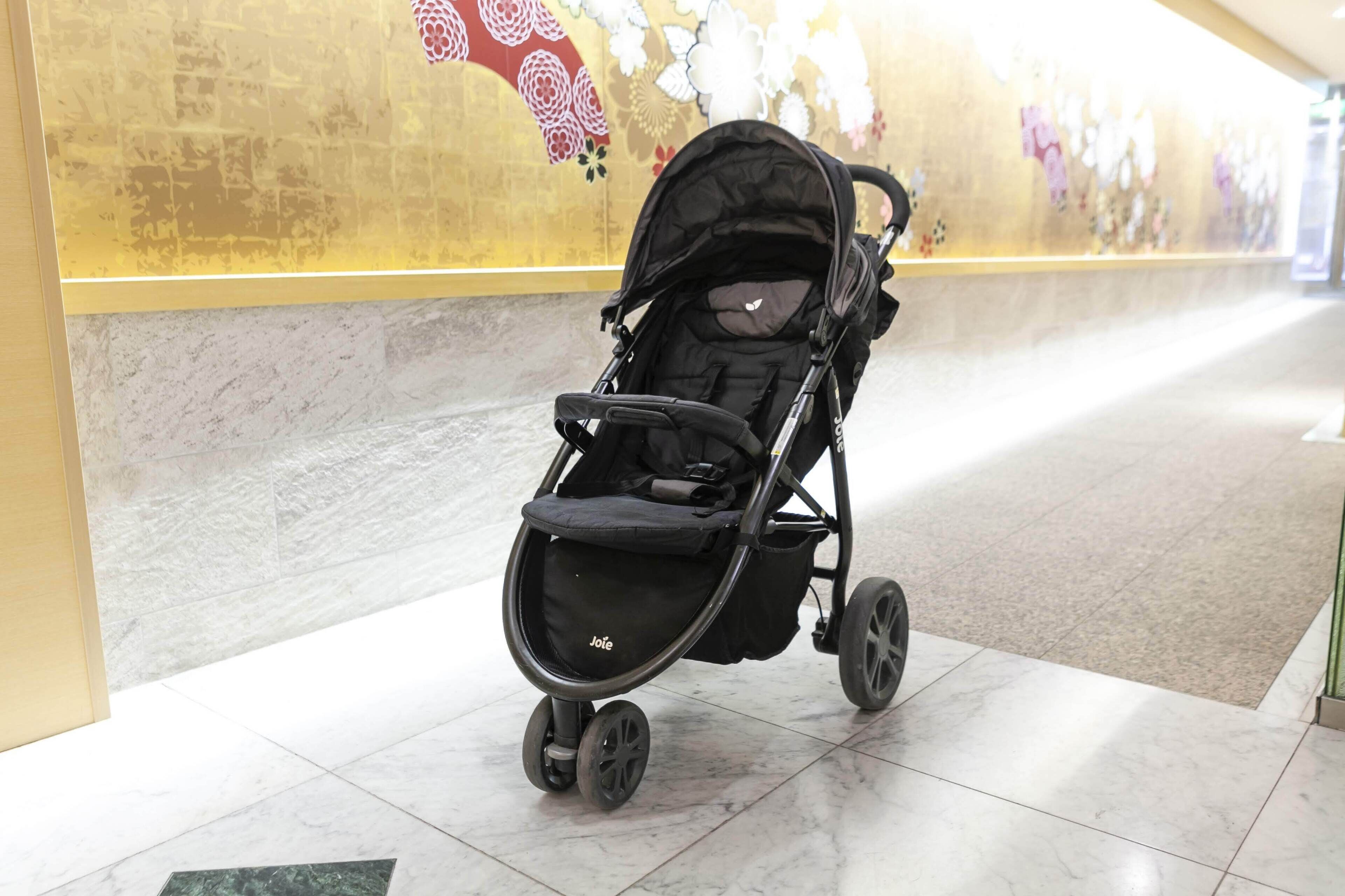 A stroller in a hallway with a tiled floor and a wall with floral patterns.