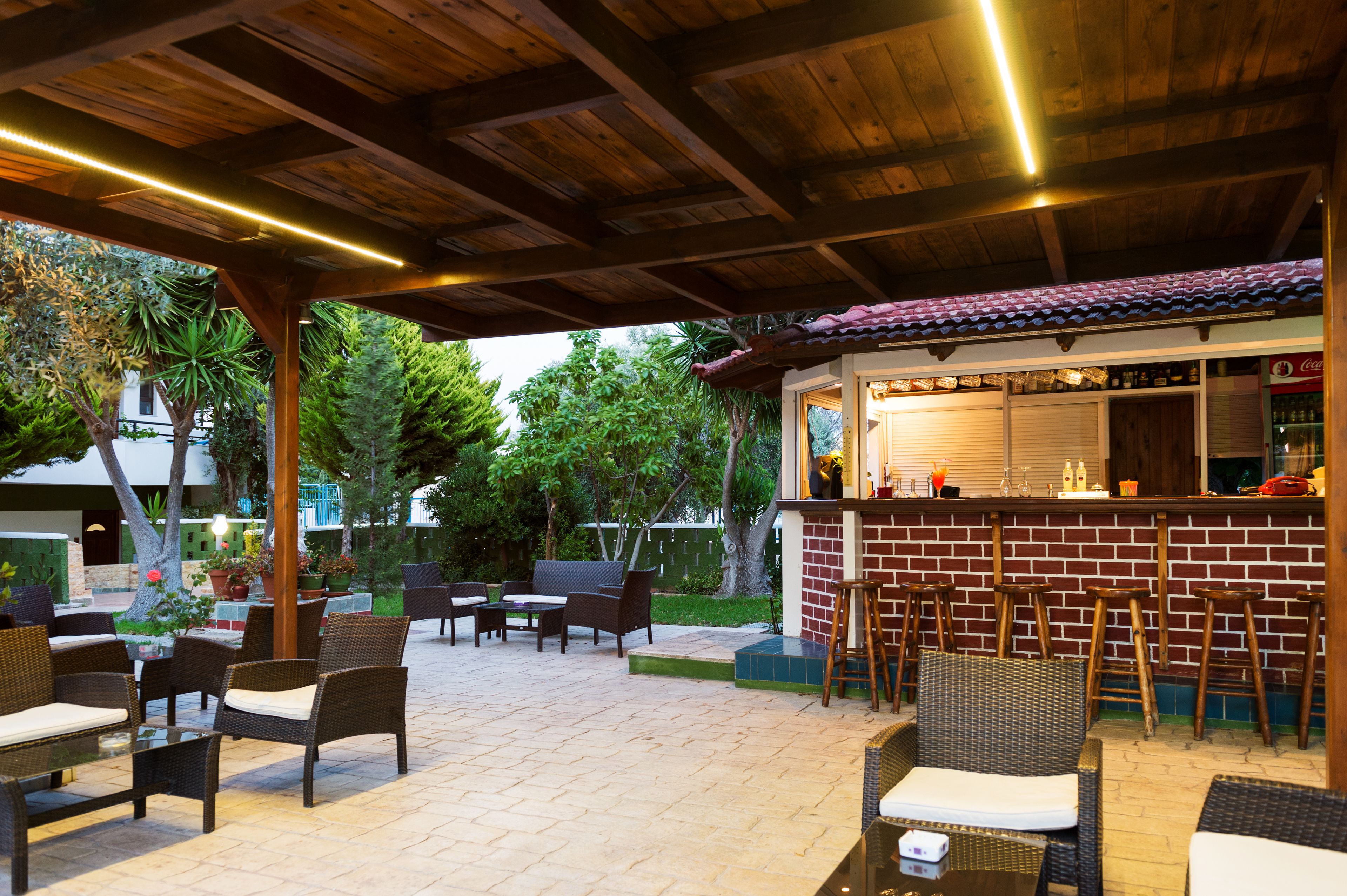 Een terras buiten met rieten meubels, een stenen bar en een houten plafond.