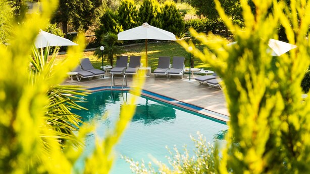 A swimming pool with lounge chairs and umbrellas, surrounded by greenery. - Terinikos Sunny Garden Hotel & Junior Suites (Rhodes)