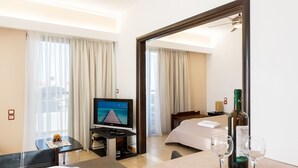 A hotel room with a bed, a TV, a dining table with two wine glasses, and a bottle of wine. - Terinikos Sunny Garden Hotel & Junior Suites (Rhodes)