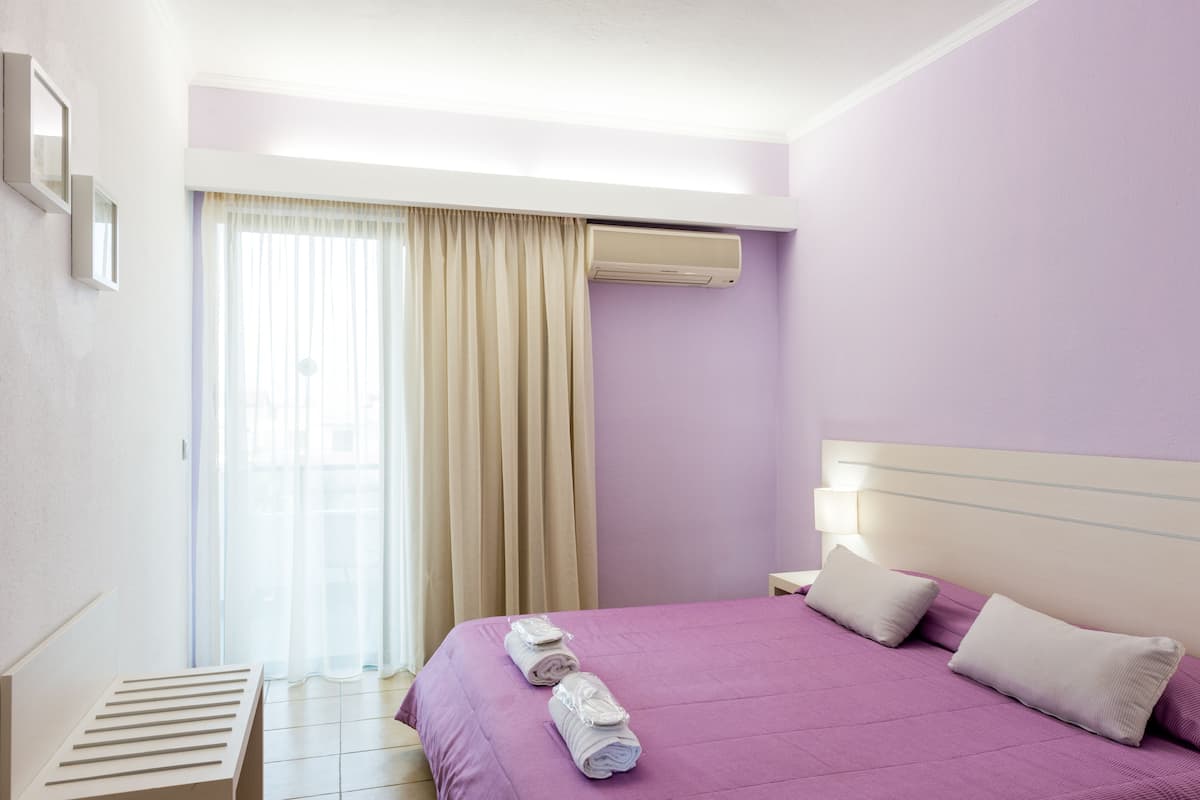 Una habitación de hotel con cama, ventana con cortinas, aire acondicionado y mesita de noche.