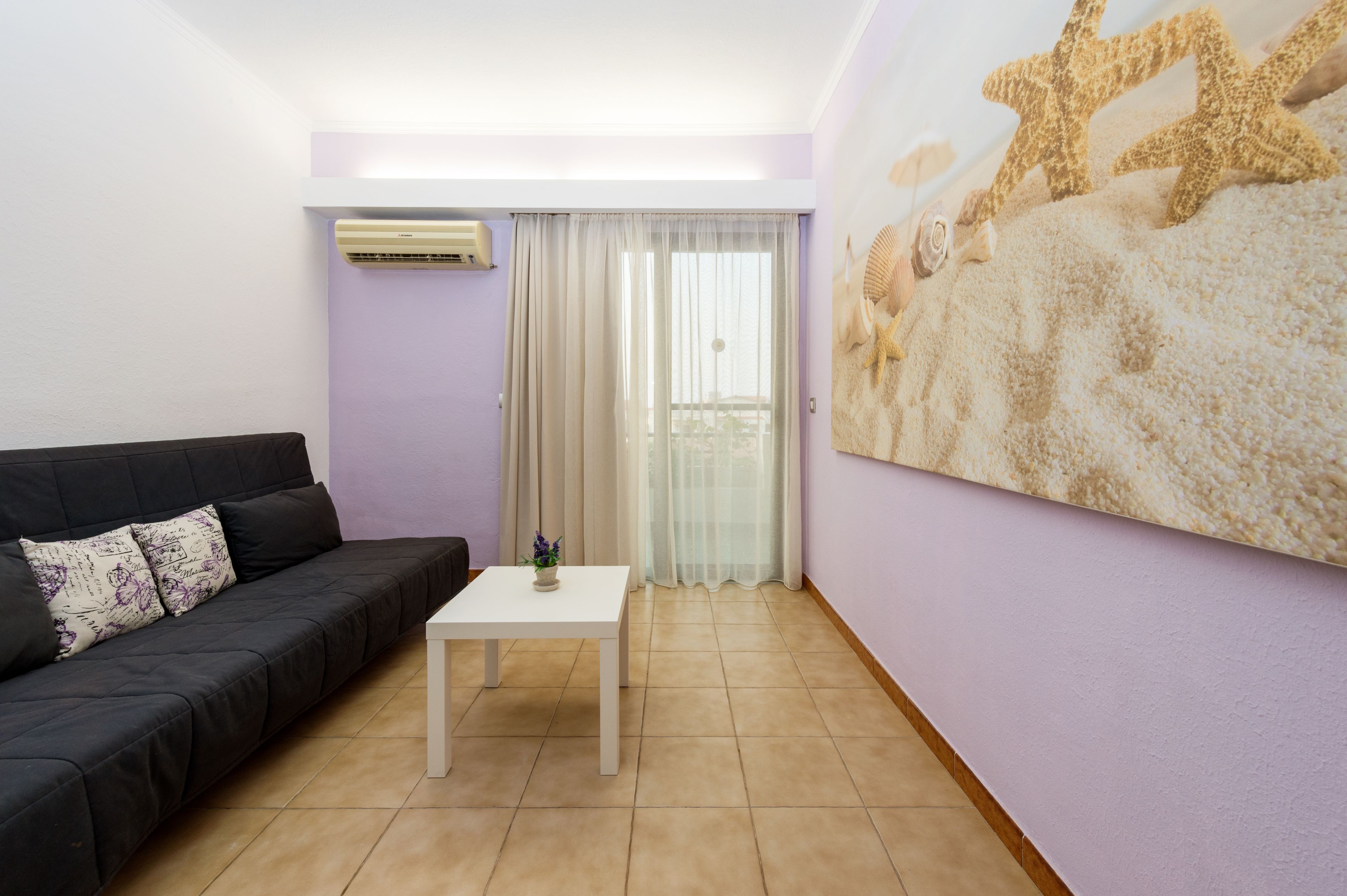 Una sala de estar con un sofá negro, una mesa blanca y un gran mural en la pared.