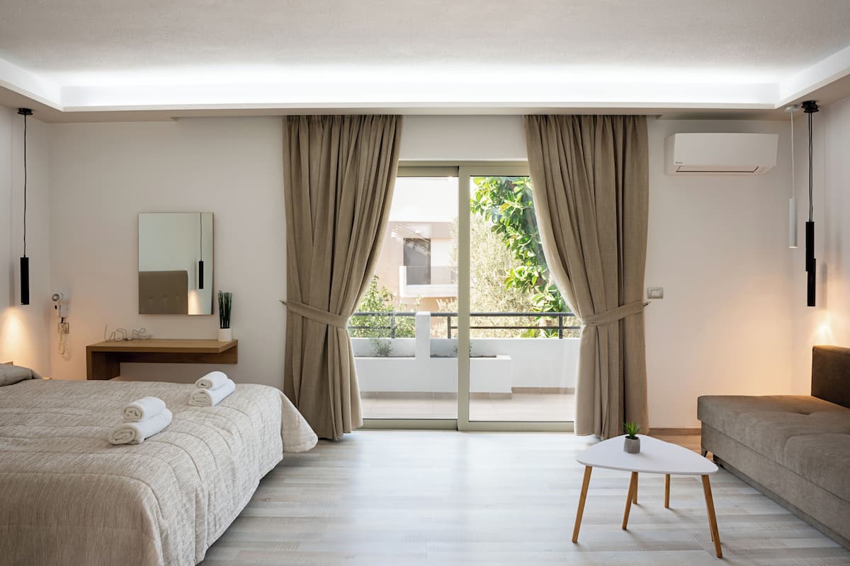 Una habitación de hotel moderna con una cama grande, una mesita, un sofá y un balcón con cortinas.