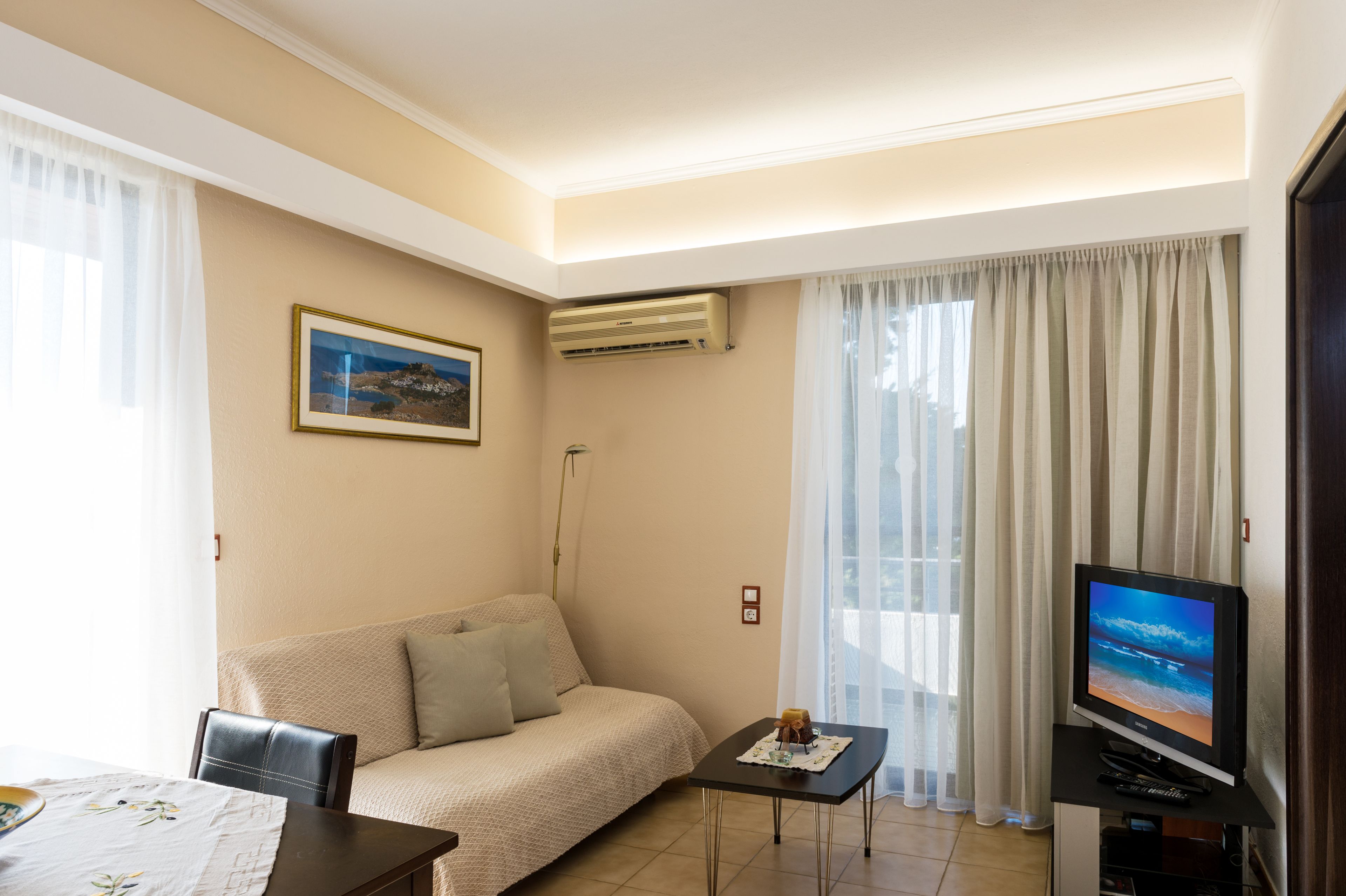 A living room with a sofa, a small table, a TV, and an air conditioning unit.