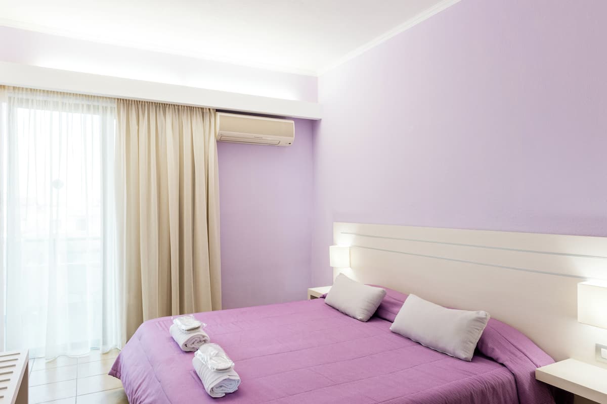 Una habitación de hotel con cama, cortinas, un equipo de aire acondicionado y una mesita de noche.