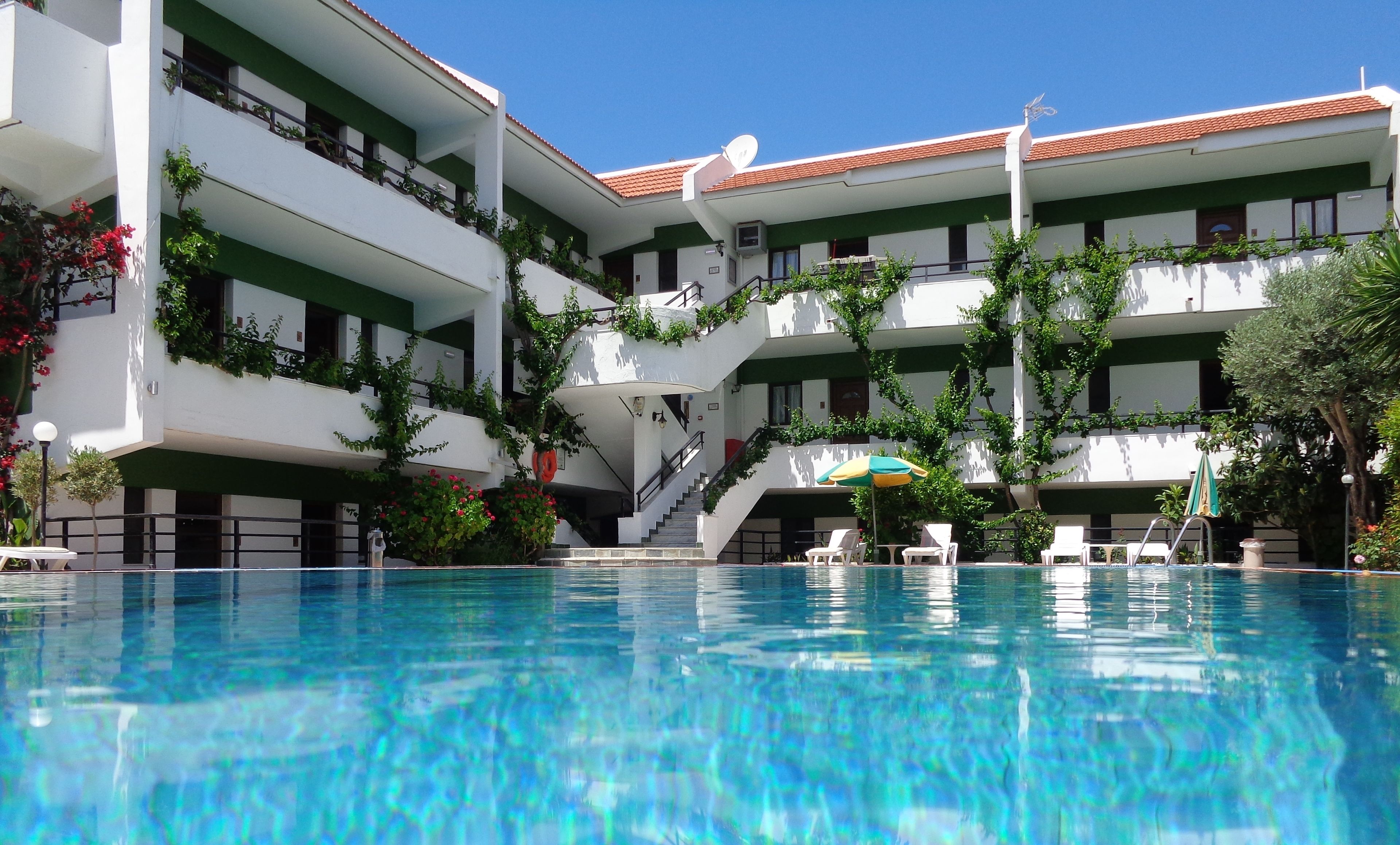 Um hotel de vários andares com piscina, área de estar externa e vegetação.