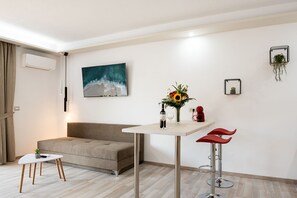 Ein modernes Wohnzimmer mit einer Couch, einem kleinen Tisch mit Vase und Weinflasche sowie einem roten Barhocker.