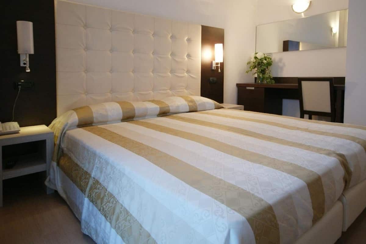 Una cama bien tendida con un edredón a rayas, una mesita de noche con una lámpara y un escritorio con una silla.