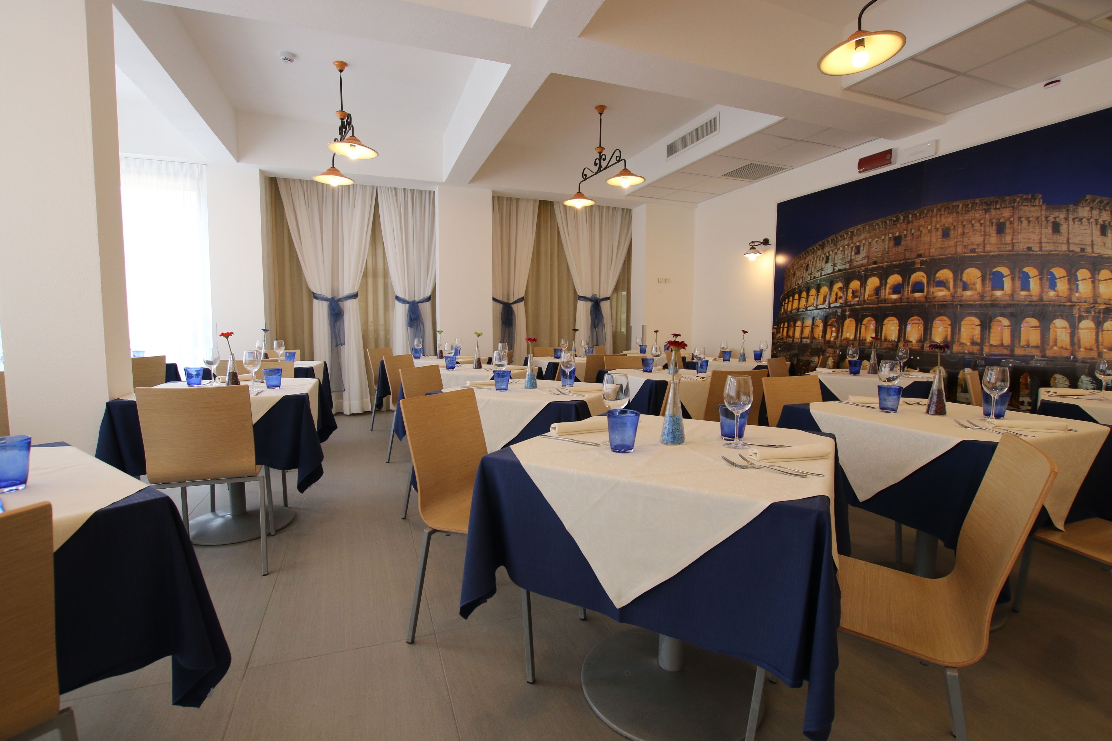 Un comedor con mesas dispuestas para el servicio, con un gran mural del Coliseo al fondo.