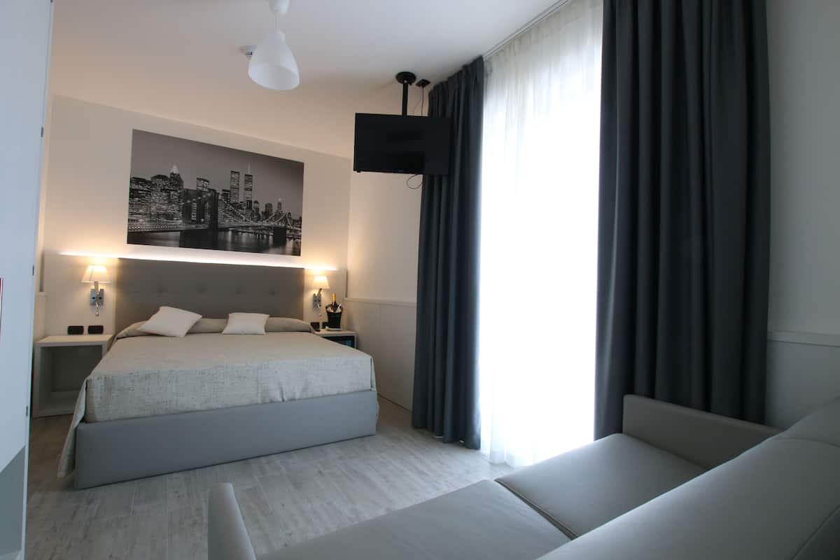 Habitación de hotel moderna con una cama grande, mesitas de noche, un televisor de pantalla plana y una obra de arte con un paisaje urbano en la pared.