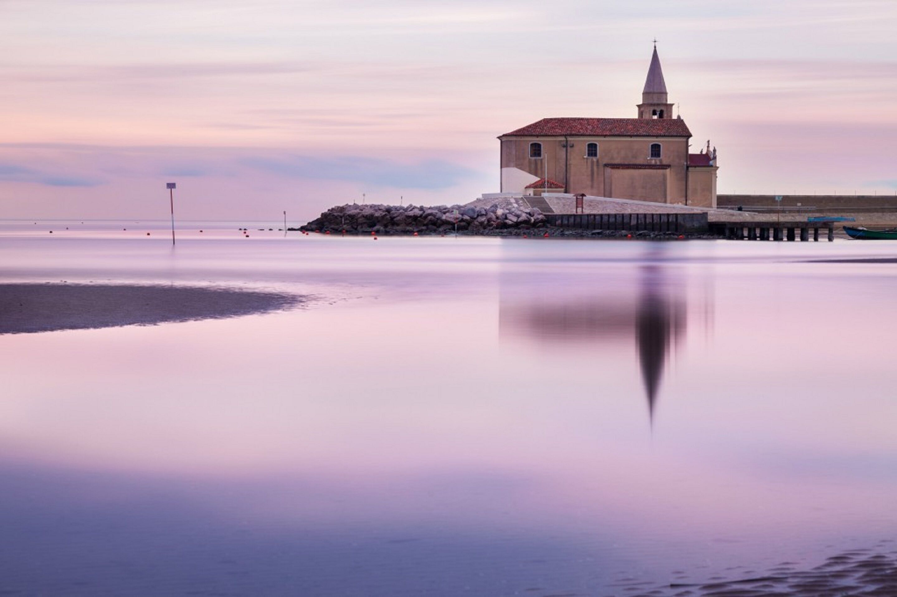 A coastal building with a tower, situated on a calm waterfront with a clear reflection.